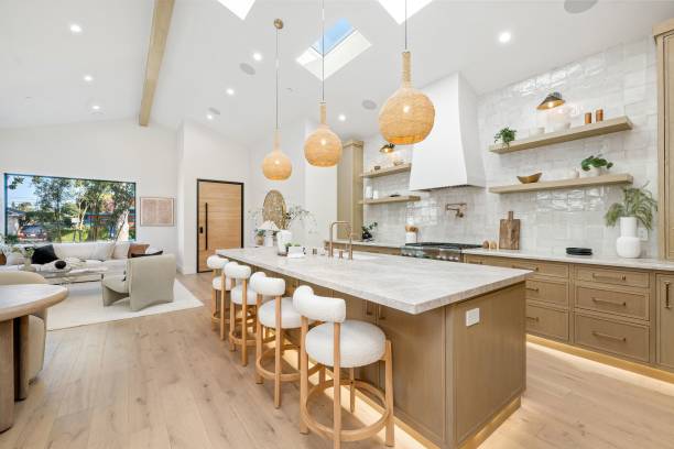 Modern kitchen interior with wooden cabinets, island, and pendant lights, featuring open shelves and a cozy living area. Done by the best company for kitchen remodeling buda TX